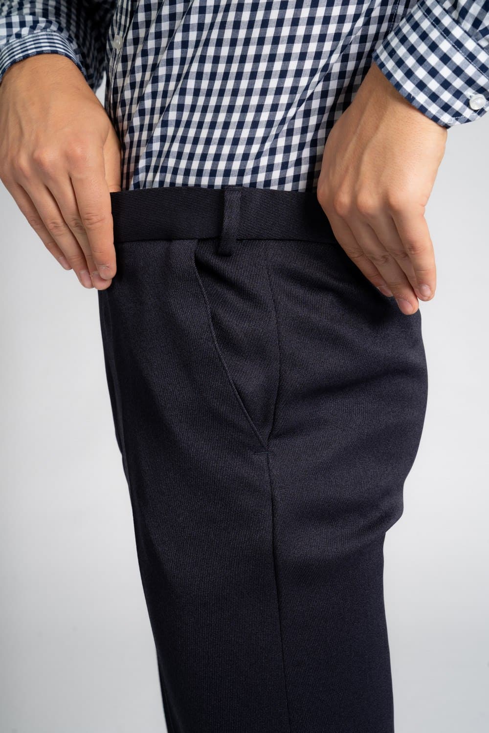 Close-up of a person wearing a blue-and-white checkered button-down shirt tucked into dark navy elastic waist pants for men, with both hands resting near the waistband.